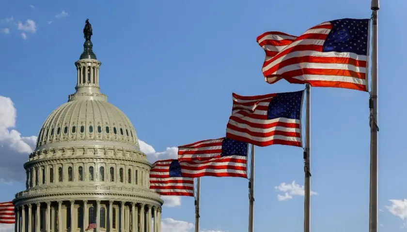 US Capitol dome with multiple American flags waving. This scene evokes patriotism, perhaps a reminder of government contracts and what is fedbizopps.