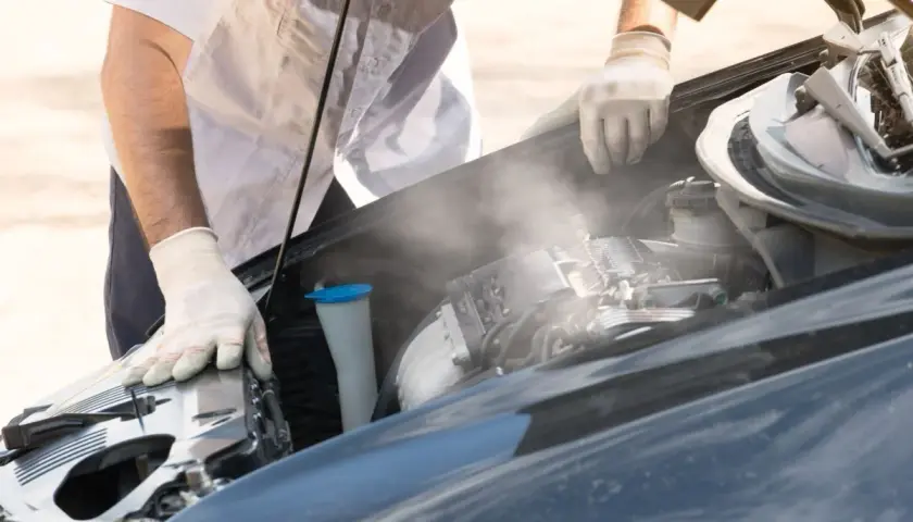 Para wylatuje z gorącego silnika po jeździe. Mechanik w rękawiczkach sprawdza auto.