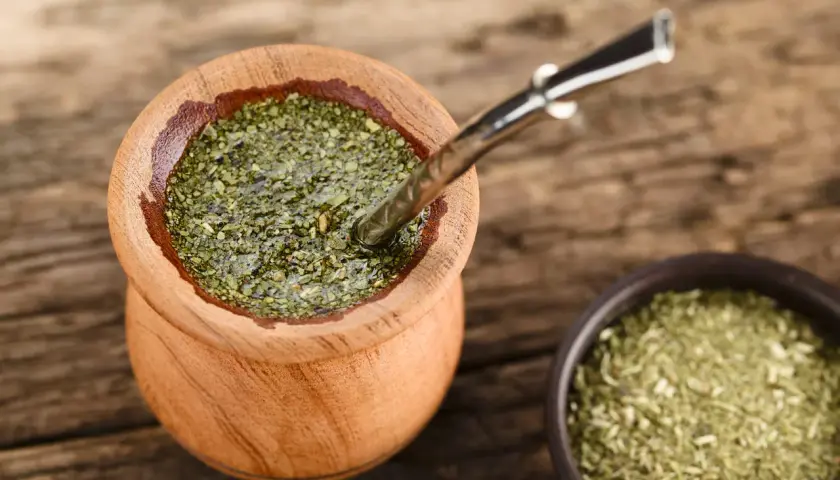 Drewniane naczynie z yerba mate na uspokojenie, obok miseczka z suszem. Metalowa bombilla zanurzona w naparze.