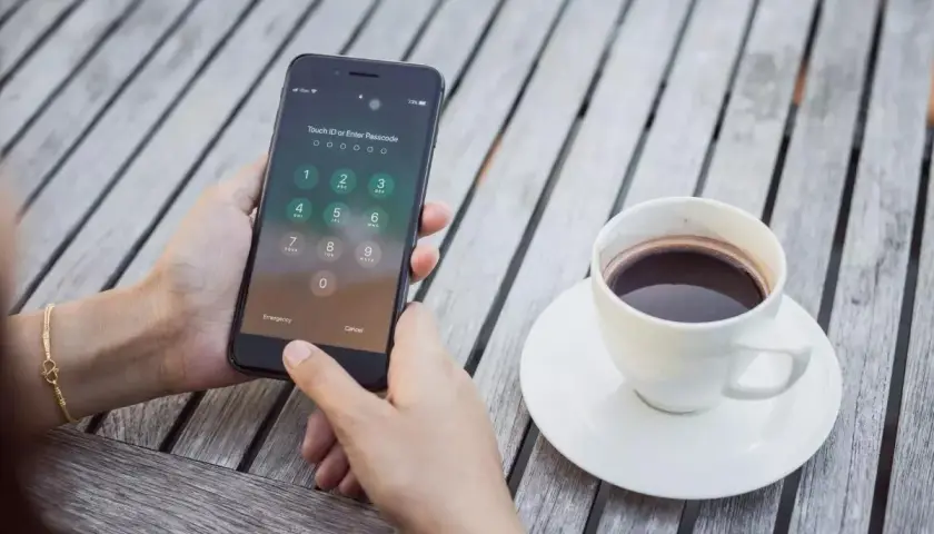 Dłoń próbuje odblokować zablokowany iPhone, obok stoi filiżanka kawy.