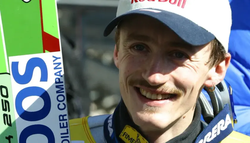 Adam Małysz w czapce Red Bull i z nartami.