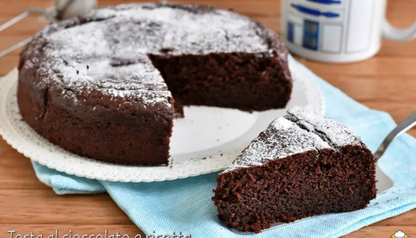 Torta al cioccolato e ricotta, soffice e golosa, spolverata di zucchero a velo. Una fetta invitante attende di essere gustata.