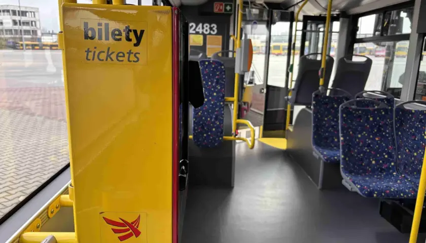 Wnętrze autobusu MPK-Łódź. Żółta skrzynka z napisem "bilety tickets" i logo MPK-Łódź. Widoczne siedzenia i poręcze.