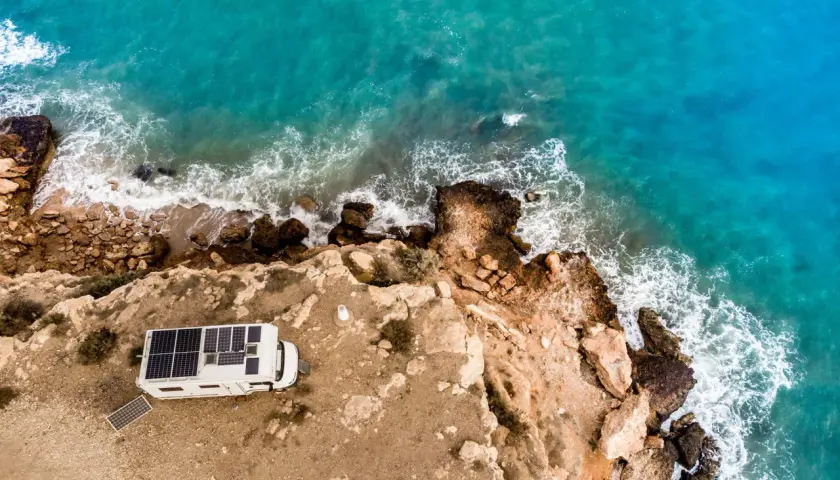Camping-car avec panneaux solaires sur une falaise en Espagne, face à la mer turquoise. Une belle escapade de camping chez l'habitant.