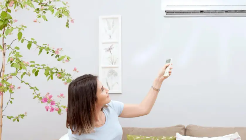 Mujer ajusta el aire acondicionado con control remoto. El vane del aire acondicionado significa confort y frescura en casa.