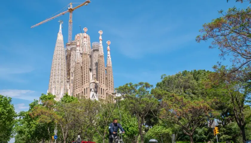 Rowerzysta mija Sagrada Familia, symbol Barcelony, podczas słonecznego dnia. Zwiedzanie tej niezwykłej budowli to marzenie wielu.