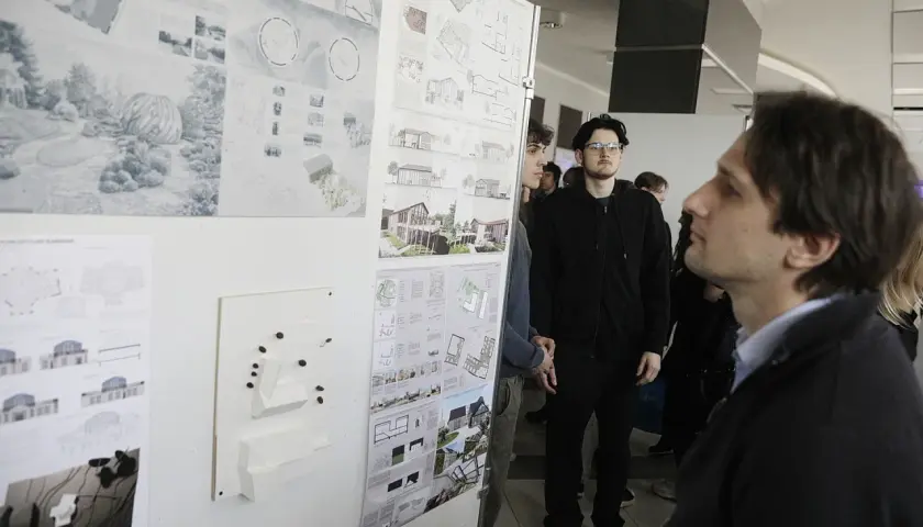 Ludzie oglądają wystawę projektów architektonicznych i makiety budynków.