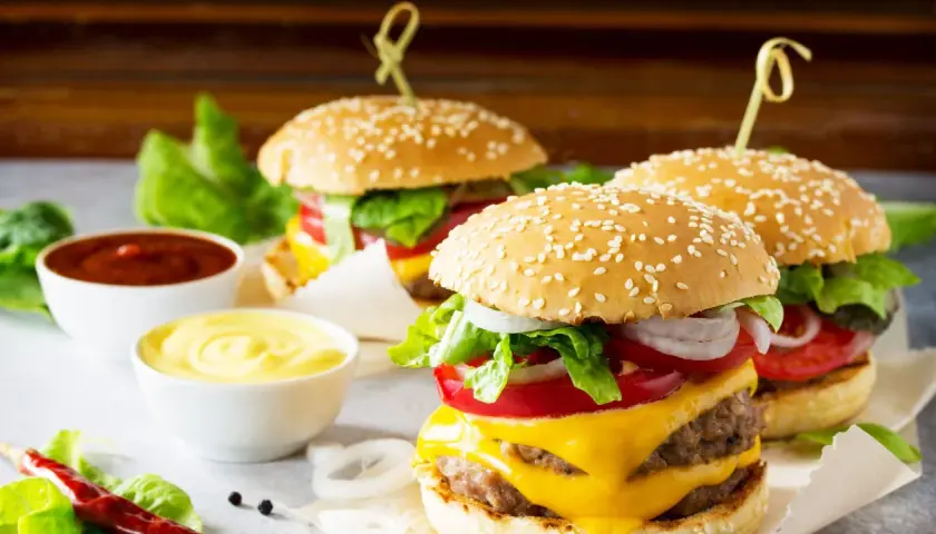 Tre succulenti burger roll con formaggio fuso, pomodoro, cipolla e lattuga, accompagnati da salse.