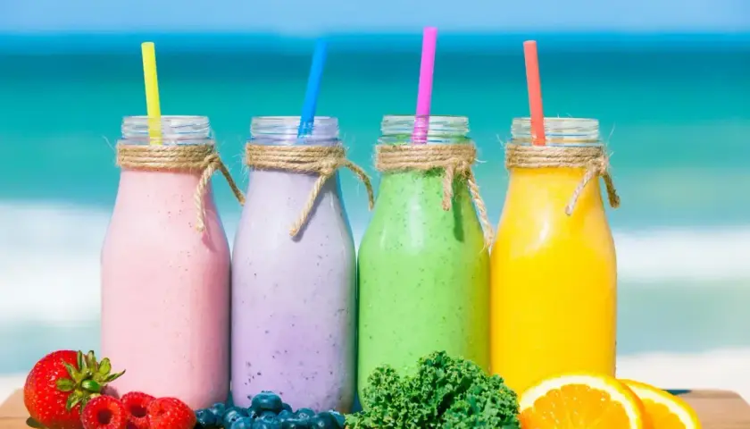 Cztery kolorowe smoothie na plaży: różowe, fioletowe, zielone i żółte. Idealne na lato, pokazują, jak zrobić smoothie z owoców i warzyw.