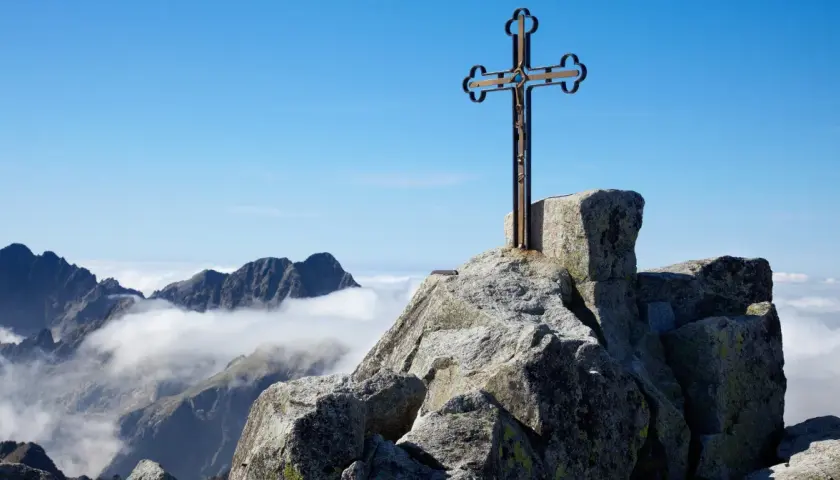 Krzyż na skalistym szczycie, najwyższy szczyt Tatr, góruje nad morzem chmur.