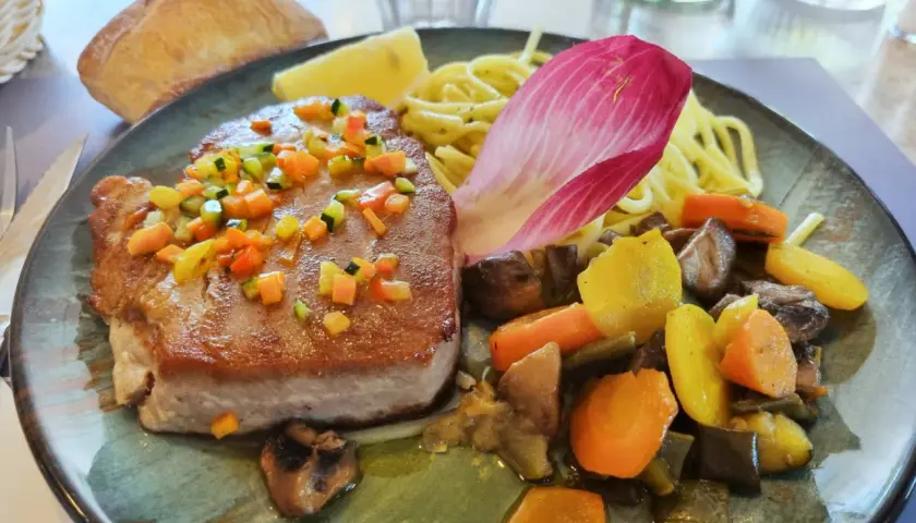 Pavé de thon poêlé, garni de dés de légumes croquants, servi avec des pâtes, des légumes racines et une feuille de chicorée. Une recette savoureuse.