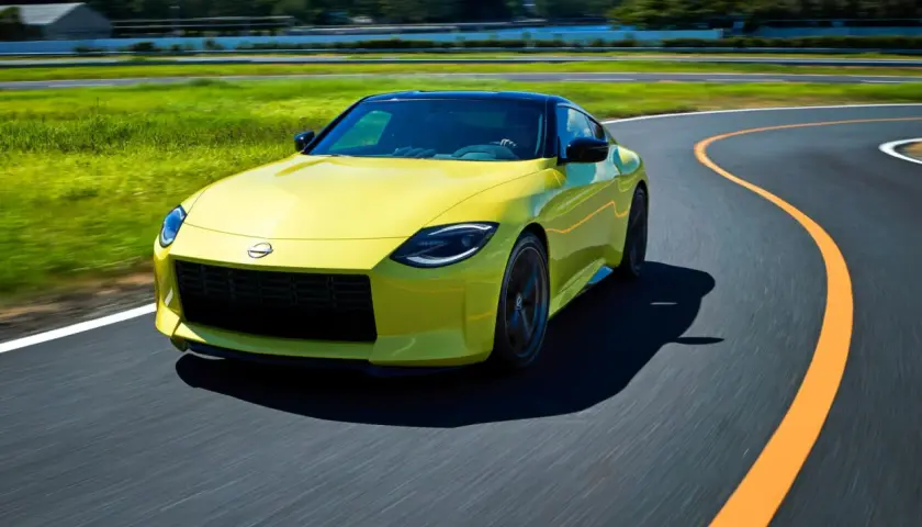 Gul Nissan 400Z kör på en kurvig bana med grönskande fält och träd i bakgrunden.