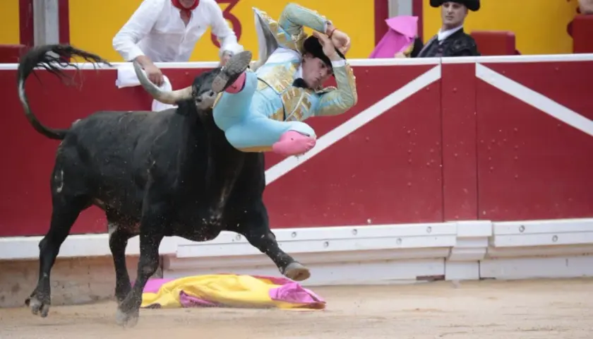 Un torero, Rubén Pinar, es lanzado por los aires por un toro negro en una plaza de toros.