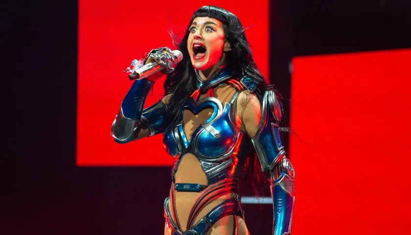 Katy Perry w błyszczącym, niebiesko-srebrnym kostiumie z sercem na piersi śpiewa na scenie w Krakowie.