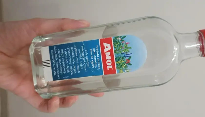 Dłoń trzyma butelkę Amolu. Ten lek, znany z dobrej ceny, zawiera mieszankę olejków eterycznych.