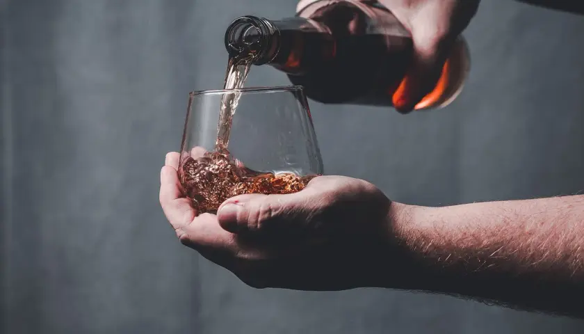 Une main verse un liquide ambré dans un verre, peut-être le pire whisky jamais goûté.