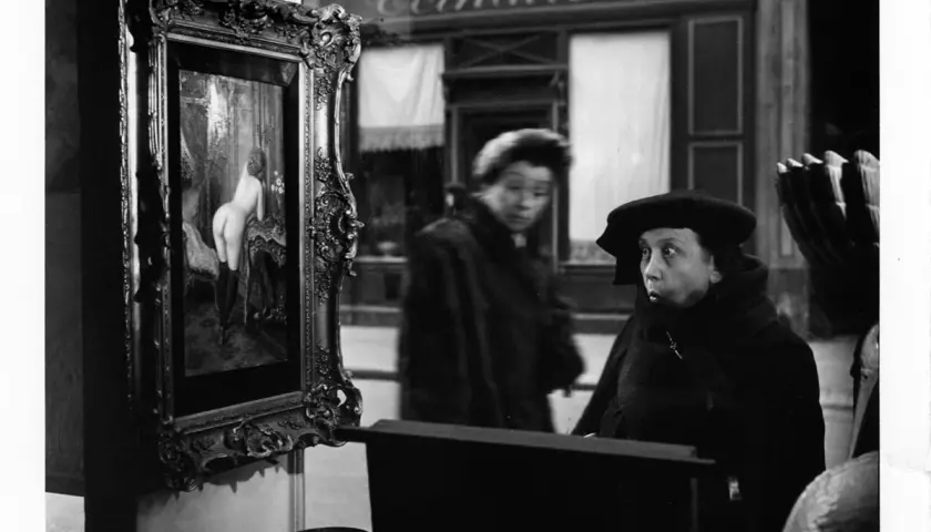 Una donna guarda un quadro in una vetrina, un'altra figura sfocata sullo sfondo. Robert Doisneau foto.