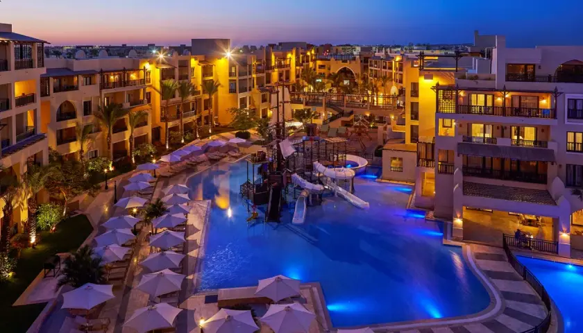 Wieczorem w Steigenberger Aqua Magic, basen z atrakcjami wodnymi i zjeżdżalniami, otoczony hotelowymi budynkami i leżakami pod parasolami.