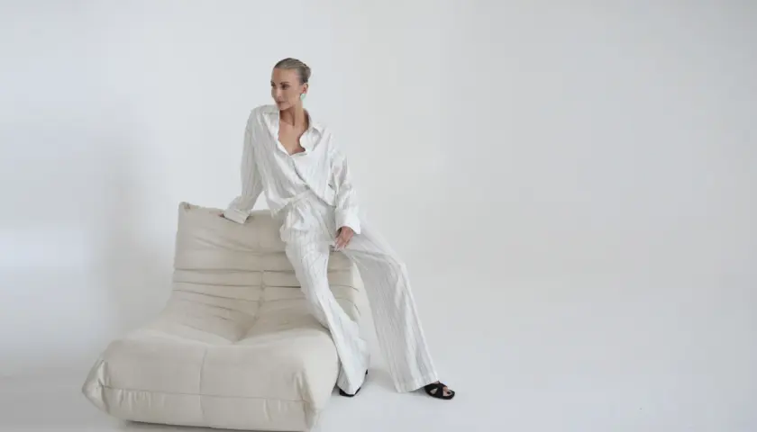 Kobieta w eleganckim, pasiastym komplecie, uosobienie quiet luxury, siedzi na kremowej sofie.