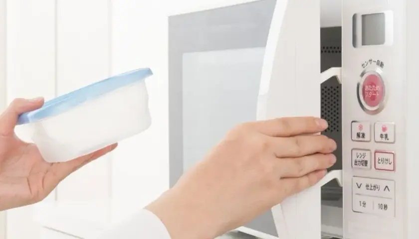Ręka wkłada pojemnik do kuchenki mikrofalowej. Ten papier w mikrofali jest gotowy do podgrzania.