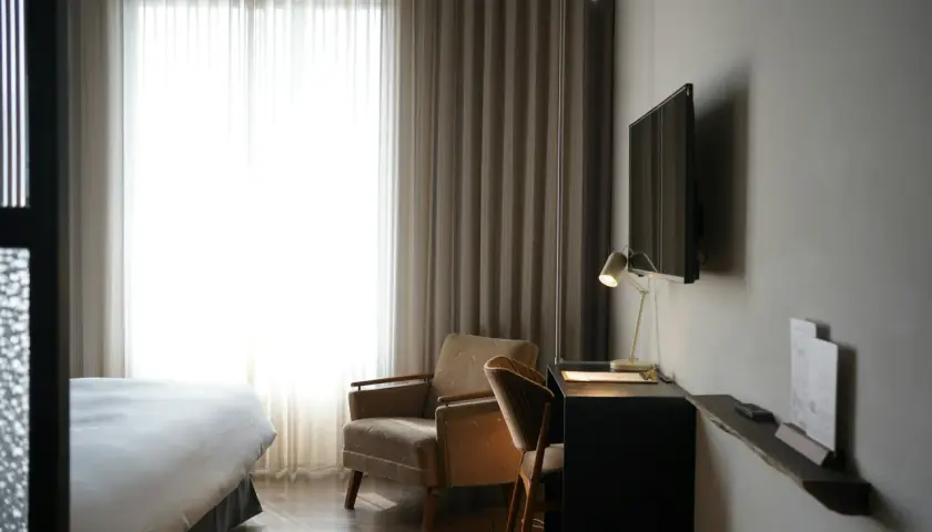 Przytulny pokój hotelowy z wygodnym łóżkiem, fotelem i biurkiem. Zastanawiasz się, ile kosztuje nocleg w takim miejscu?