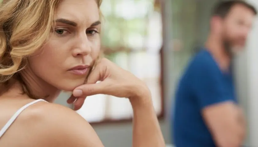 A woman looks worried, with a man blurred in the background.