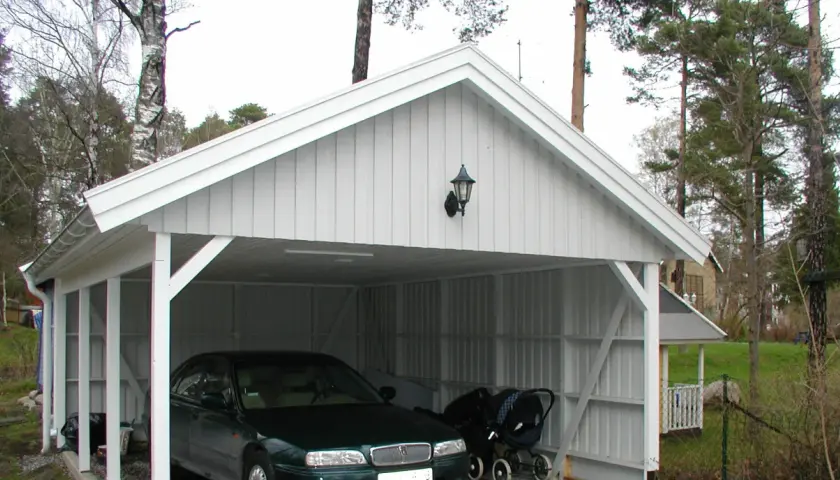 Vit carport på plintar med en bil och barnvagn.