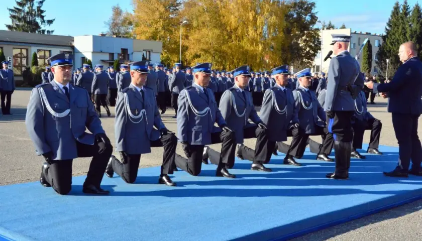 Uroczystość policyjna, policjanci w mundurach klęczą na niebieskim dywanie.