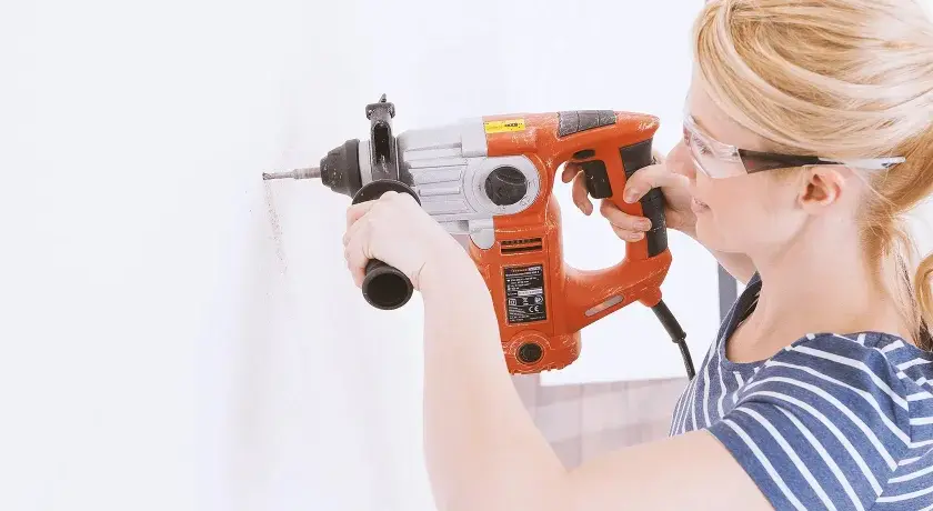 Femme avec lunettes de protection utilisant un marteau-perforateur pour percer du béton.
