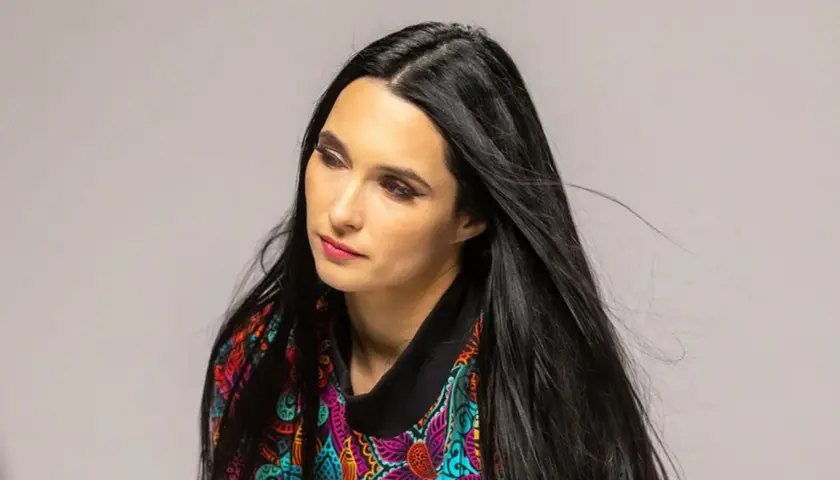 Portret kobiety z długimi, czarnymi włosami w kolorowej bluzce. Emilia Sanecka, data urodzenia.