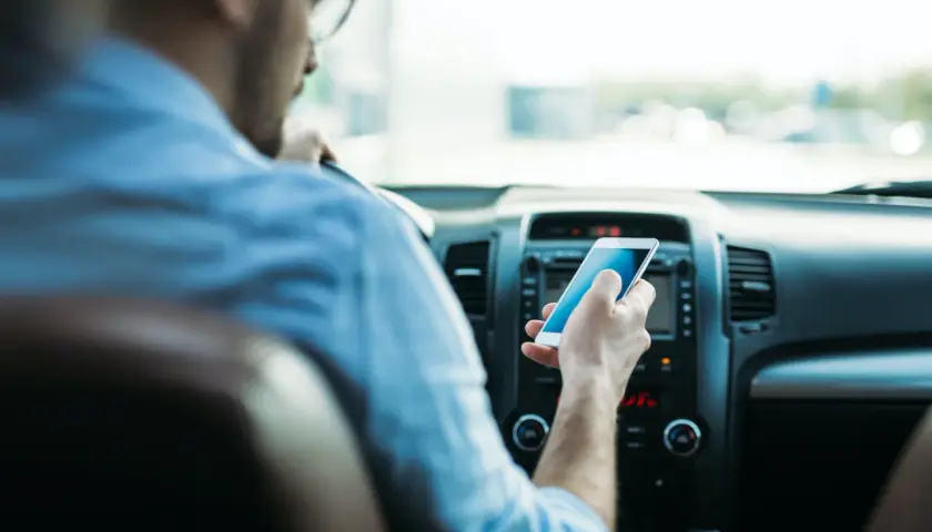 Mężczyzna w okularach trzyma telefon, sprawdzając wiadomości. Widok zza kierowcy, jakby przez lustro.