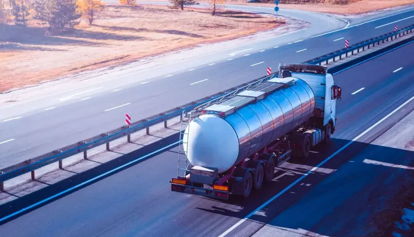 Ein Tankwagen transportiert **Gefahrgut ADR** auf einer Autobahn. Der LKW fährt auf der rechten Spur, die Sonne wirft lange Schatten.