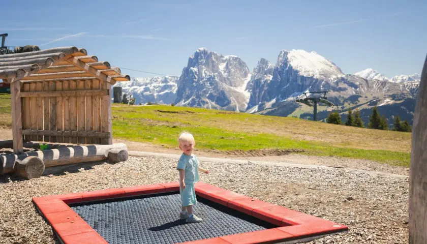 Mały chłopiec na trampolinie na tle majestatycznych gór we Włoszech.