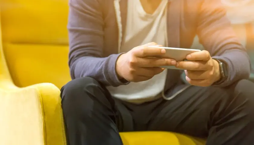 Mężczyzna siedzi na żółtym fotelu, grając na telefonie. Nawet poza siecią, jego **tuya smart** urządzenia działają bez zarzutu.