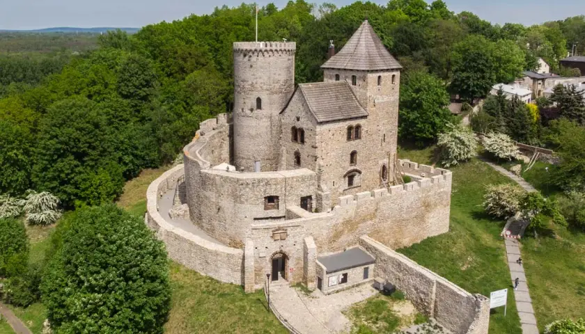 Kamienny zamek na wzgórzu, otoczony murami i zielenią. Jeden z najpiękniejszych zamków w Polsce, zapraszający do odkrywania historii.