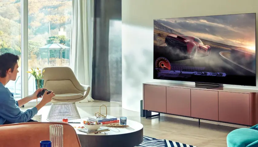 Młody mężczyzna gra w grę wyścigową na telewizorze 65 cali. Idealna odległość od telewizora 65 cali zapewnia wciągające wrażenia.