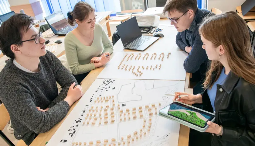 Studenci architektury analizują projekt urbanistyczny z makietą i planami.