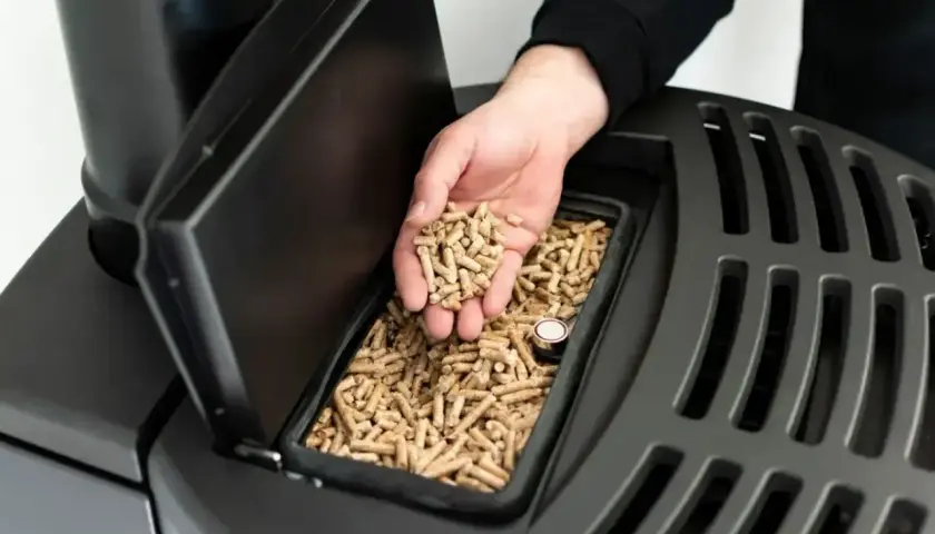 Dłoń wsypuje pellet do zasobnika. Kocioł na pellet praca ciągła zapewnia ciepło przez długi czas.