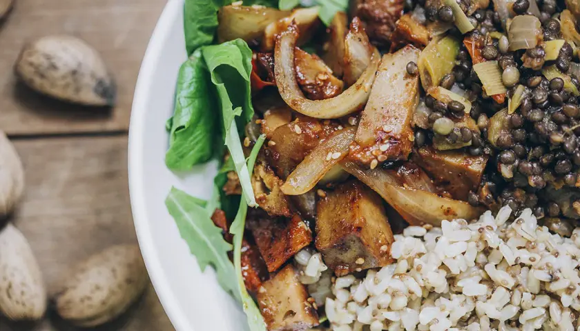 Plato con seitan salteado, lentejas, arroz integral y hojas verdes. Una deliciosa opción para tus recetas de seitan.