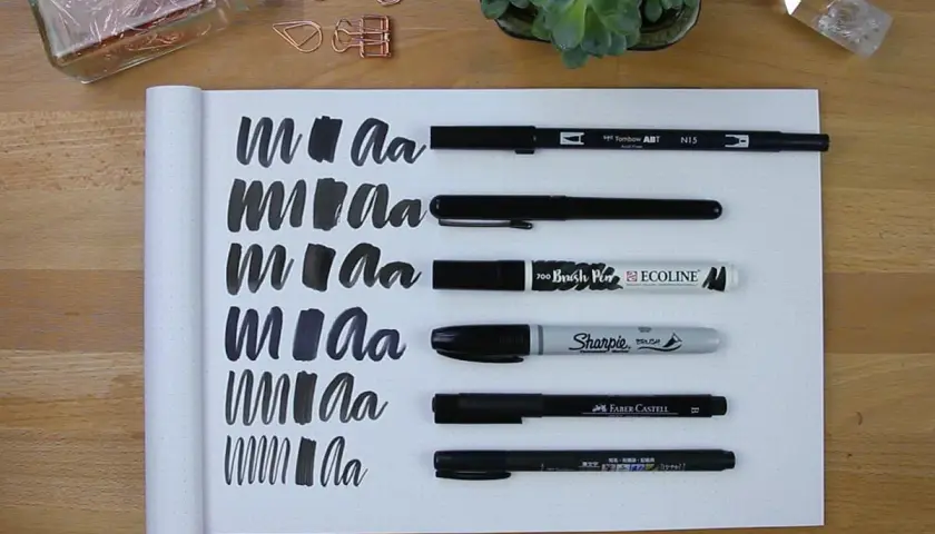 Práctica de lettering con varios rotuladores, mostrando trazos y letras "m" y "a" en un cuaderno.