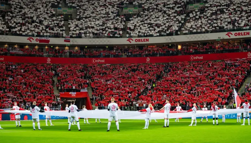 Piłkarze reprezentacji Polski mężczyzn z biało-czerwoną flagą na murawie. Trybuny wypełnione kibicami tworzą biało-czerwone mozaiki, wspierając rankingi reprezentacji.