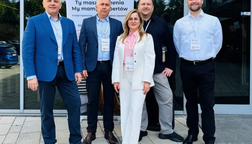 Pięć osób w eleganckich strojach stoi przed budynkiem, na tle banera z logo "m Finanse".