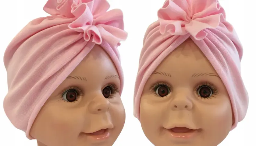 Uroczy, różowy turban dla noworodka z ozdobnym kwiatkiem na czubku głowy.