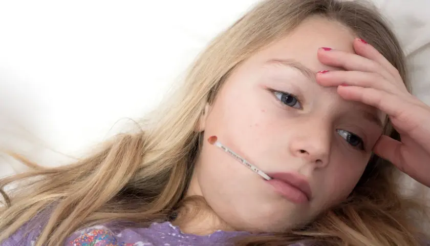 Une jeune fille malade avec un thermomètre dans la bouche, se demandant combien de temps dure la mononucléose.