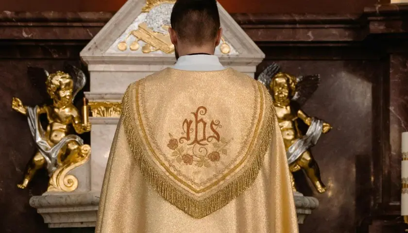 Kapłan w złotej kapie z symbolem IHS. Złote aniołki po bokach ołtarza. Zastanawiasz się, ile trwa msza święta?