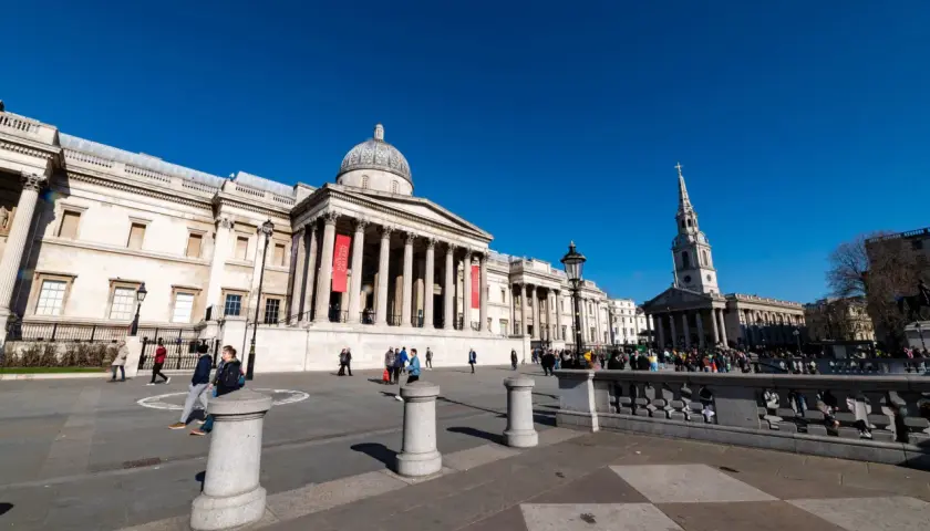 Trafalgar Square w Londynie, z National Gallery w tle. Wiele osób spaceruje po placu, ciesząc się darmowymi muzeami Londyn.