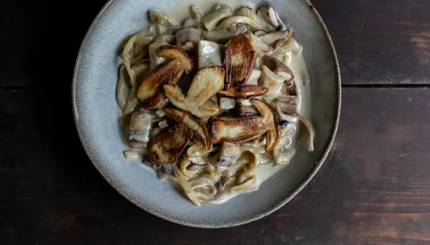 Cremige Spaghetti mit gebratenen Pilzen, ein köstliches italienisches Gericht, serviert in einer rustikalen Schüssel auf dunklem Holz.