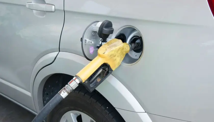 Żółta dysza dystrybutora paliwa wlewana jest do baku srebrnego samochodu. Prosty sposób, jak zatankować auto.