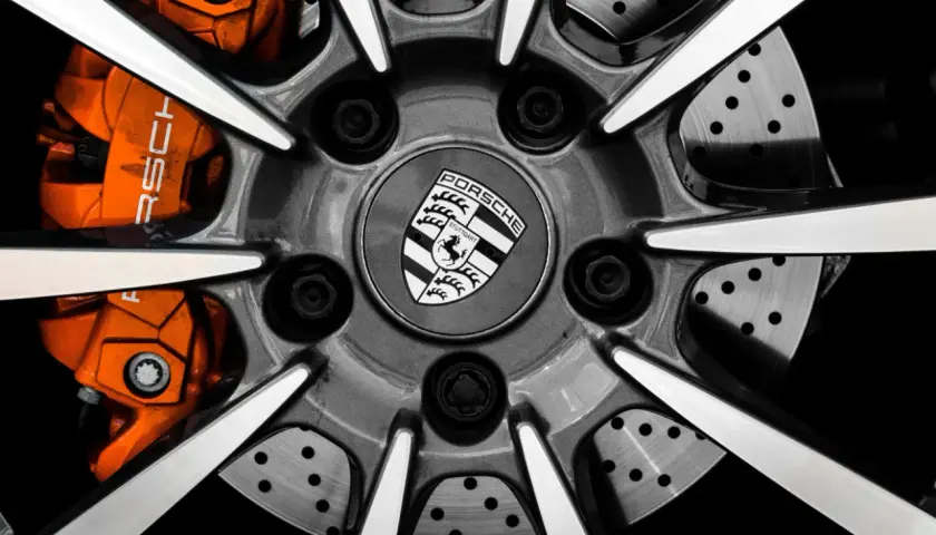 Zbliżenie na felgę Porsche z pomarańczowymi zaciskami hamulcowymi i logo marki.