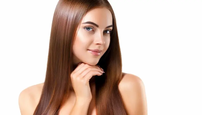 Mujer con cabello largo y liso, color de pelo avellana con reflejos dorados, sonríe suavemente.